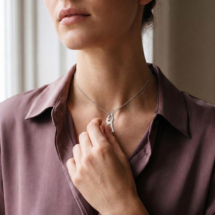 Figure Skater Necklace worn with a mauve button-front blouse, showing the overhead hand-held skate silhouette at the neckline