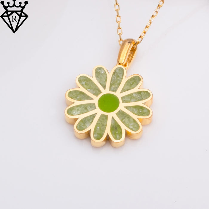 Front product close-up of a green-petal daisy pendant on a gold-toned chain against a white background
