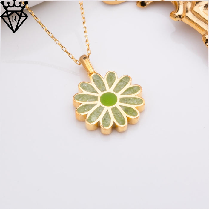 Product close-up of the green-petal daisy pendant on a gold-toned chain with partial unrelated jewelry visible at the upper edge
