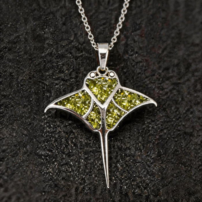 Front close-up of the Peridot Manta Ray Necklace with green stone-detail sections, swept wings, circular cutouts, and a tapered tail on dark fabric