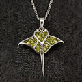Front close-up of the Peridot Manta Ray Necklace with green stone-detail sections, swept wings, circular cutouts, and a tapered tail on dark fabric