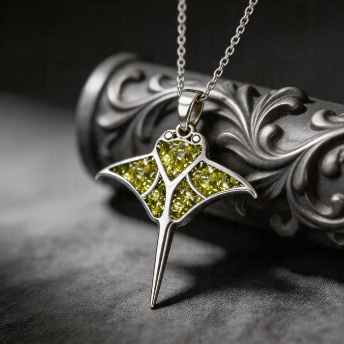 Peridot Manta Ray Necklace with green stone-detail sections beside a dark ornamental object