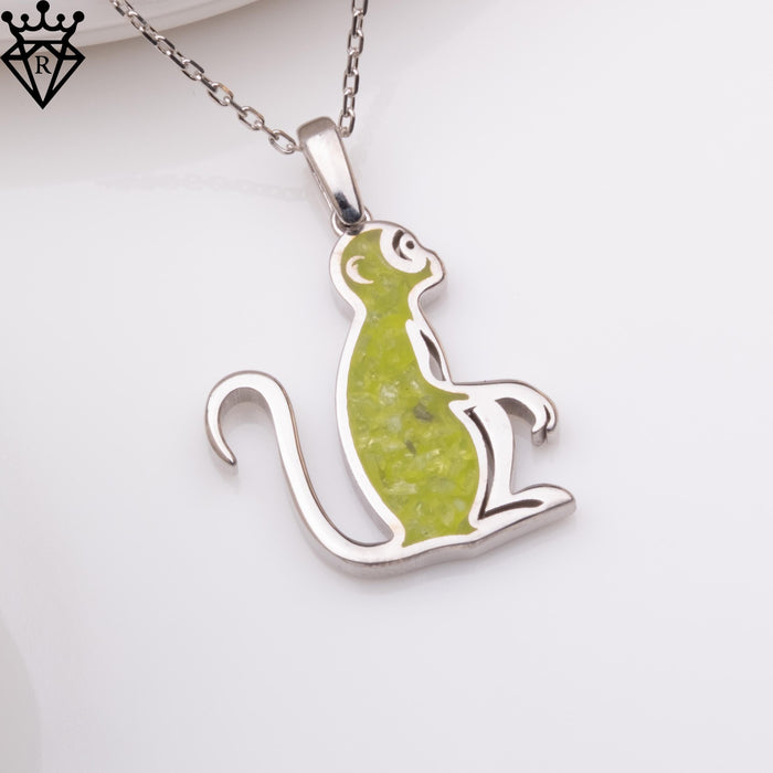 Angled close-up of the matching seated monkey pendant with green center detail and curled tail. A black crown-and-diamond logo watermark appears in the upper-left corner
