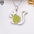 Close product photograph of a seated squirrel pendant on a chain with a green body detail and a gold decorative prop