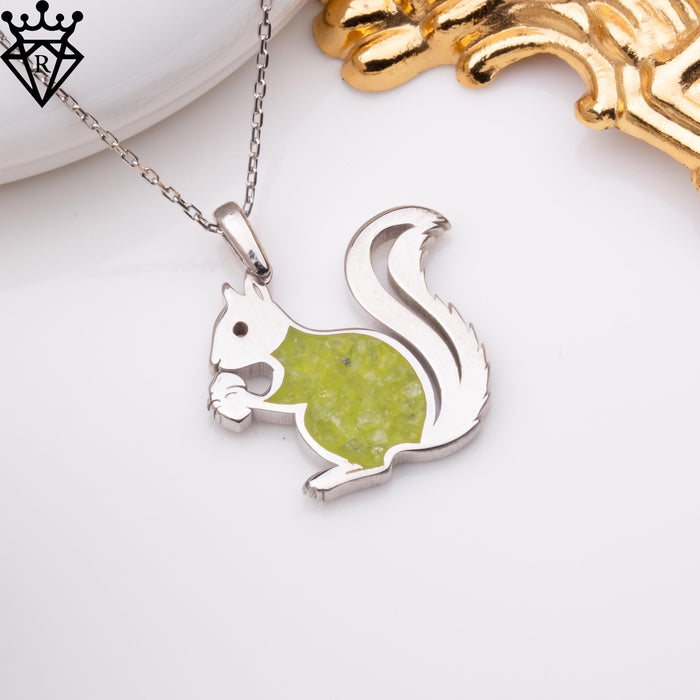 Product flat lay of the squirrel pendant on a chain beside a white ceramic dish and gold decorative prop