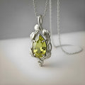 Silver leaf-and-vine pendant with a green pear-shaped stone on a neutral surface