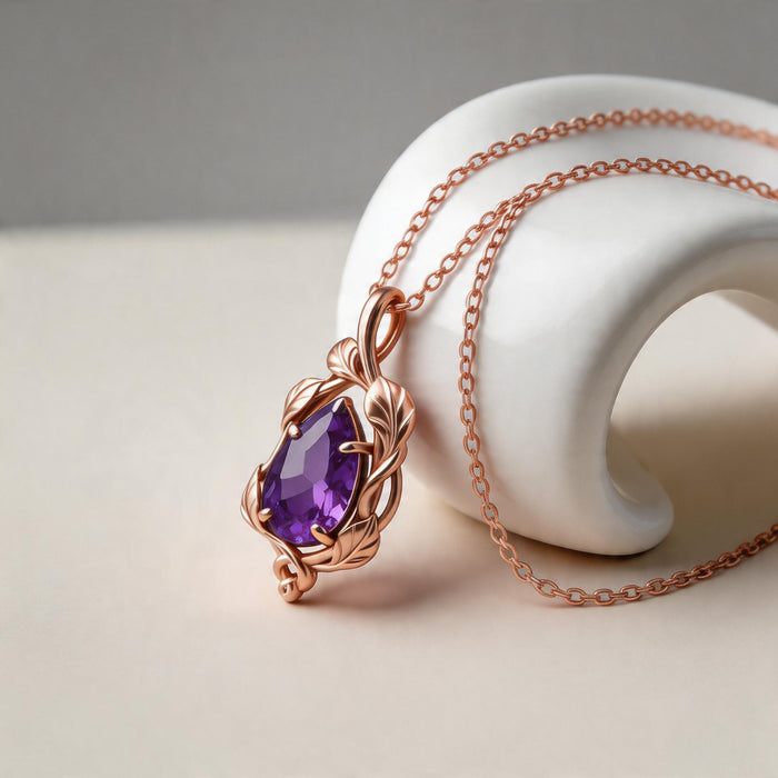 Rose-toned leaf-and-vine pendant with a purple pear-shaped stone on a white display stand