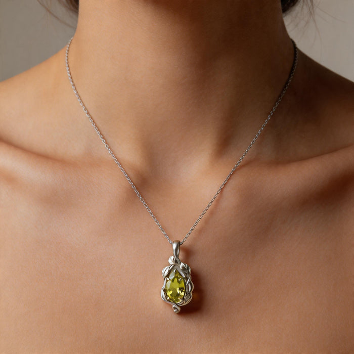 Close worn view of a silver leaf-and-vine pendant with a green pear-shaped stone