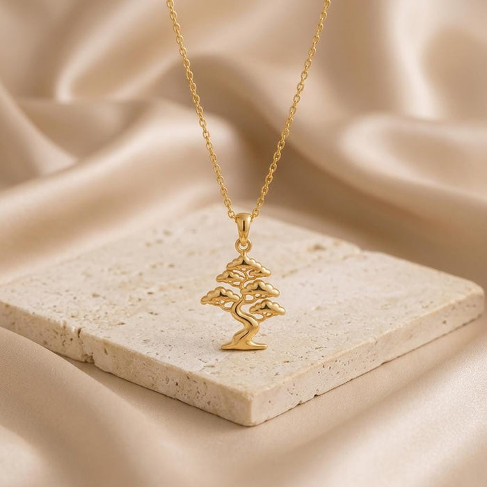 Gold Plated Silver Pine Crest Bonsai Pendant necklace displayed on a light stone tile