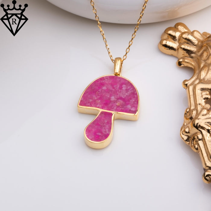 Gold-tone necklace chain arranged beside the pink mushroom charm and white dish
