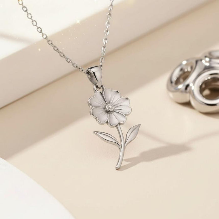 Silver Primrose Flower Pendant Necklace displayed beside silver jewelry on a cream surface