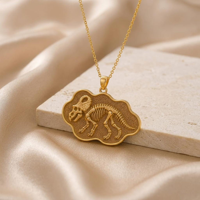 Gold Plated Silver Protoceratops skeleton relief pendant displayed on a stone slab