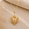 Gold Plated Silver Queen Seraph Crest Pendant with a crowned shield and feathered wings on beige fabric