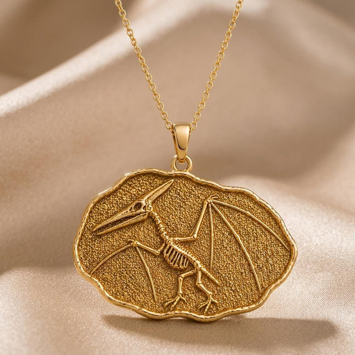 Gold Plated Silver Quetzalcoatlus Fossil Pendant Necklace with a winged skeleton in an irregular textured frame on beige fabric