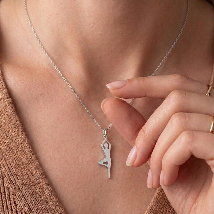 Raised-leg yoga figure necklace worn with a tan knit cardigan