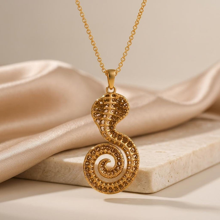 Gold Plated Silver Sacred Cobra Fossil Necklace with a coiled tail beside satin and a stone slab