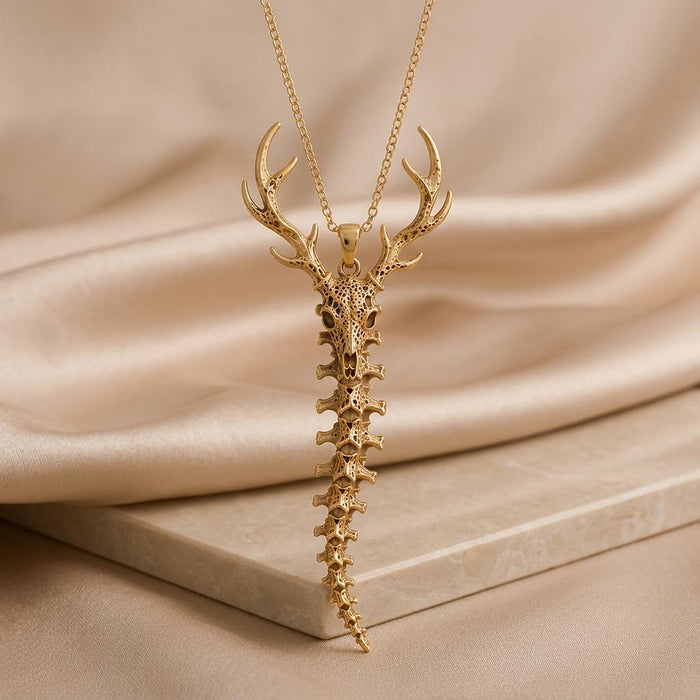 Gold Plated Silver Sacred Deer Spine Necklace with deer skull and tapered vertebrae pendant above a stone slab