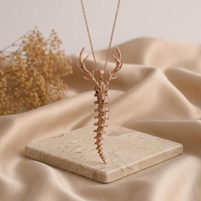 Rose-toned Sacred Deer Spine Necklace with antlered skull and vertebrae pendant on a pale stone platform