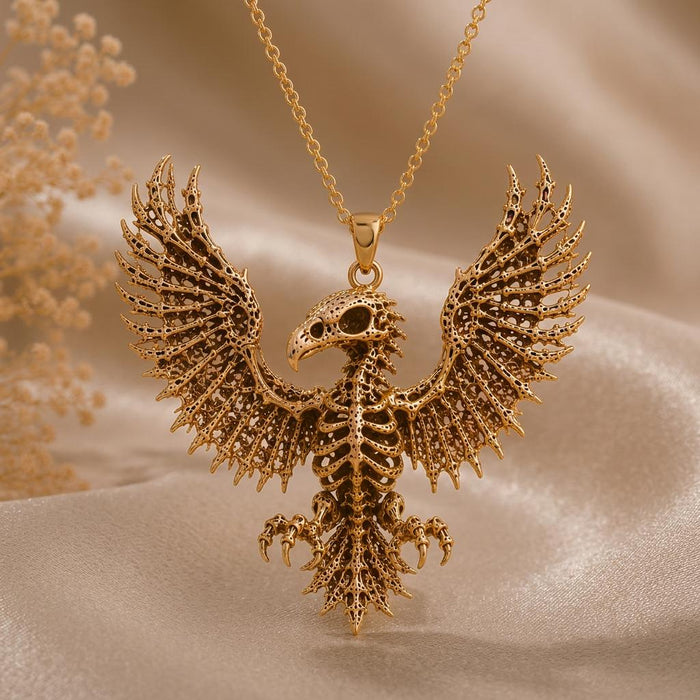 Gold-toned Sacred Eagle Skeleton pendant suspended above champagne satin with dried flowers at the left edge