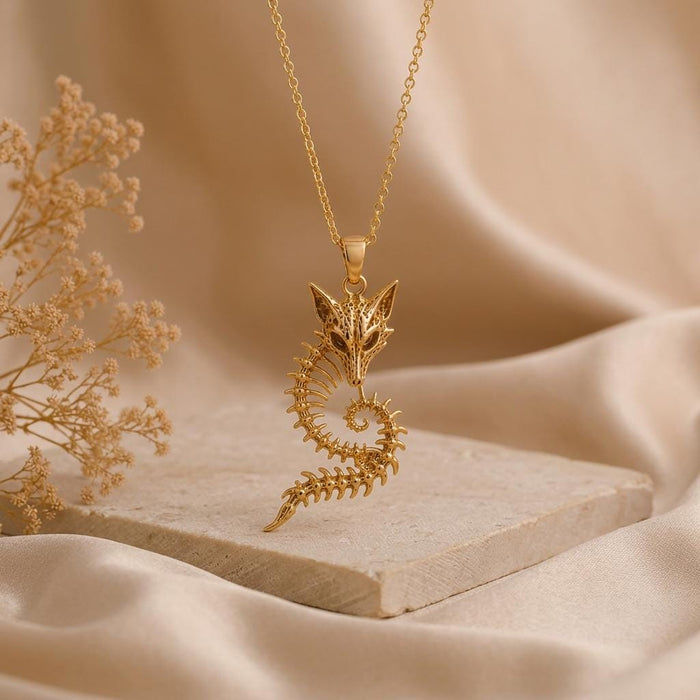 Gold Plated Silver Sacred Fox Skeleton Crest Pendant hanging above a stone slab beside dried flowers