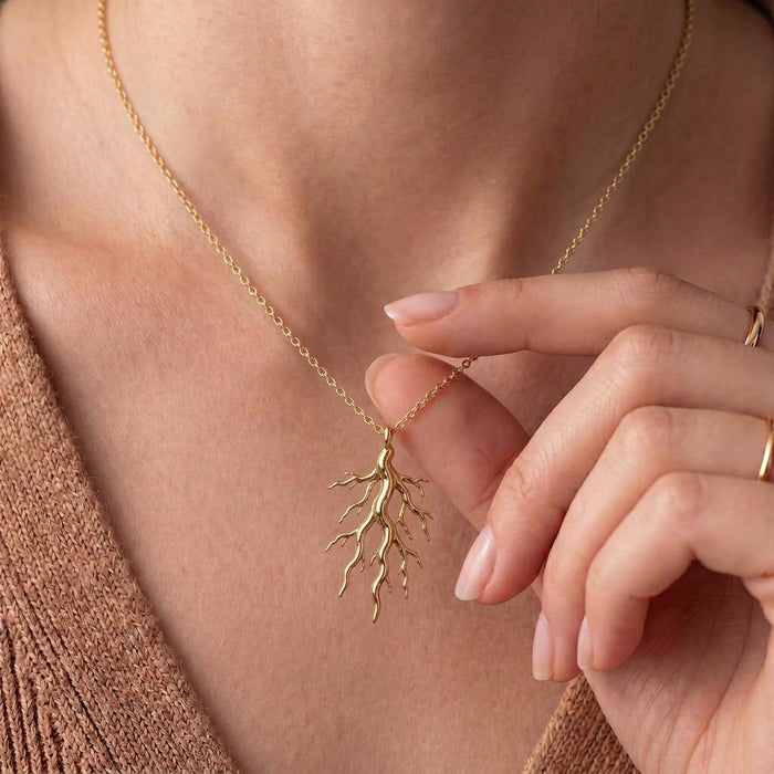 Gold Plated Silver Sacred Root Necklace worn at the neckline with a hand holding the pendant