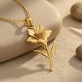Gold Plated Silver Saffron Flower Pendant Necklace with pointed layered petals, curved stem, and two leaves on a textured neutral surface
