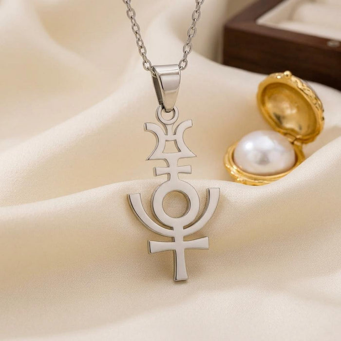 Silver Serapis symbol pendant on cream satin beside an open gold-colored locket