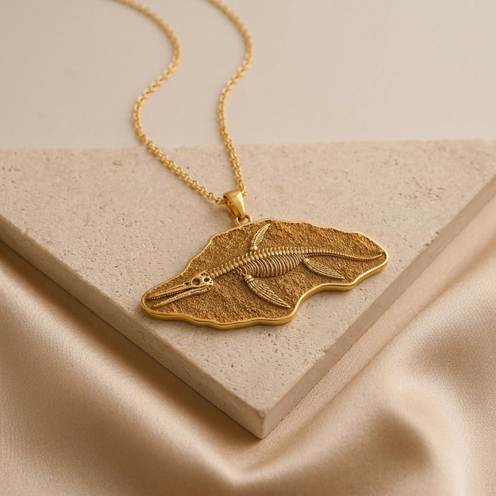 Gold Plated Silver Shonisaurus fossil pendant resting on a pale stone slab