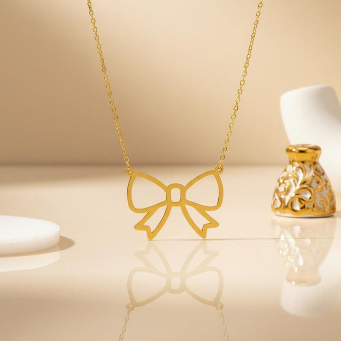 Gold Plated Silver Bow Pendant Necklace displayed upright above a reflective cream surface