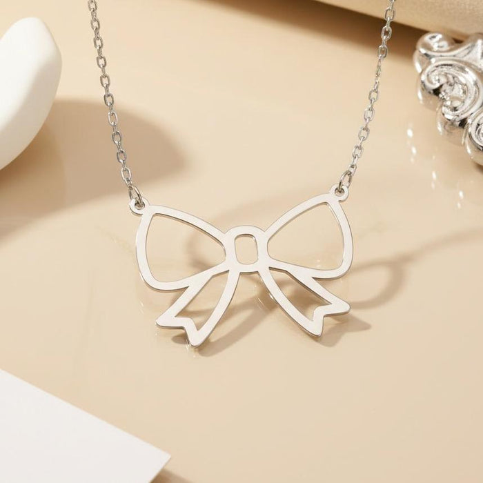 Silver Bow Pendant Necklace close-up on a cream surface with decorative objects