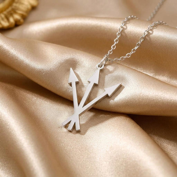 Angled close-up of the triple-arrow pendant and chain on champagne satin
