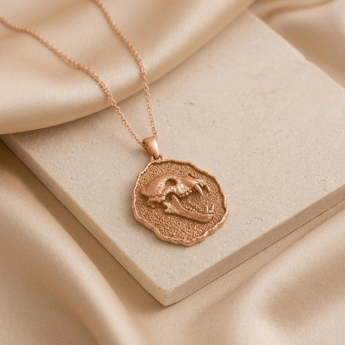 Rose Gold Plated Cave Bear Fossil Pendant Necklace displayed on a stone block with satin