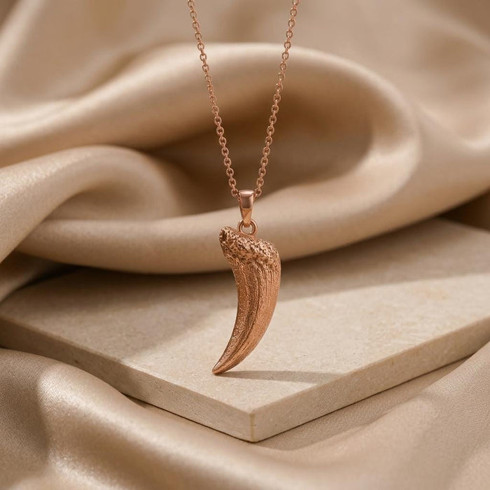 Rose Gold Plated Smilodon fang fossil pendant necklace on a stone display with champagne satin