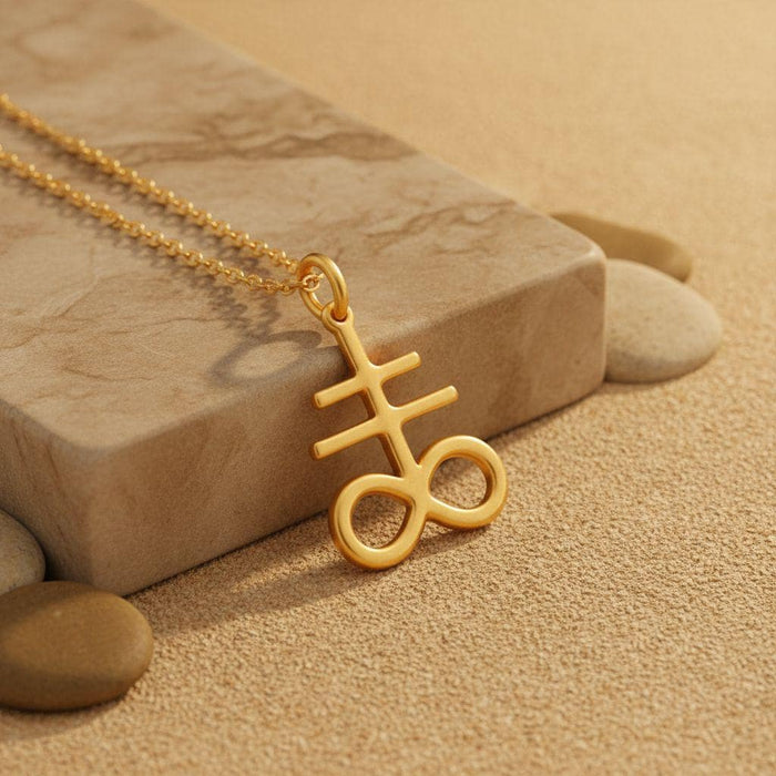 Gold Plated Silver Leviathan Cross pendant close-up on a stone block surrounded by sand