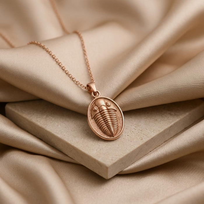 Rose Gold Plated trilobite pendant necklace on champagne satin and a stone block