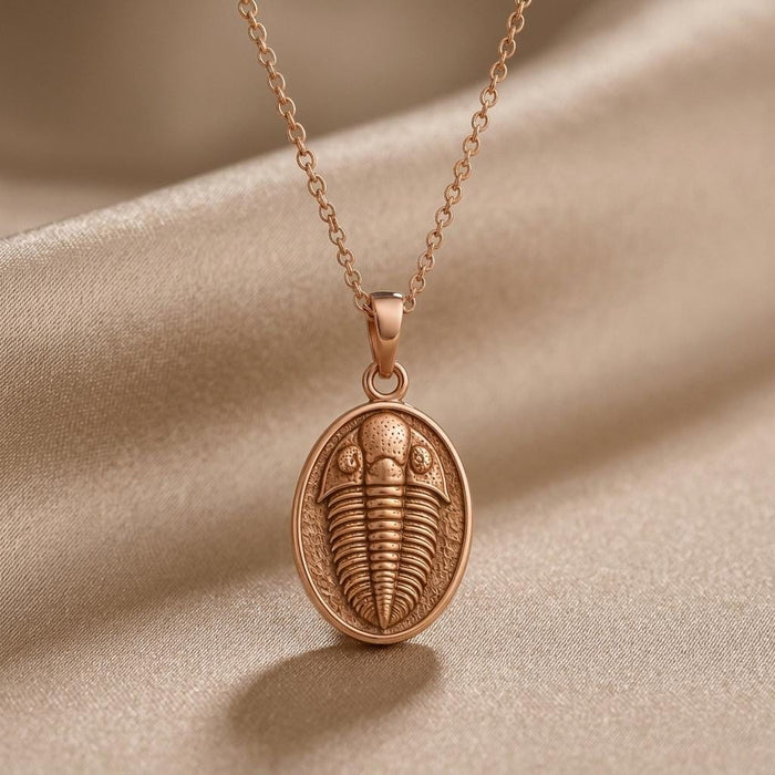 Close-up of Rose Gold Plated trilobite relief pendant on champagne satin