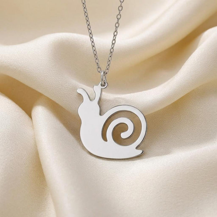 Close-up of the silver snail pendant with raised antennae and an open spiral-shell cutout on ivory satin