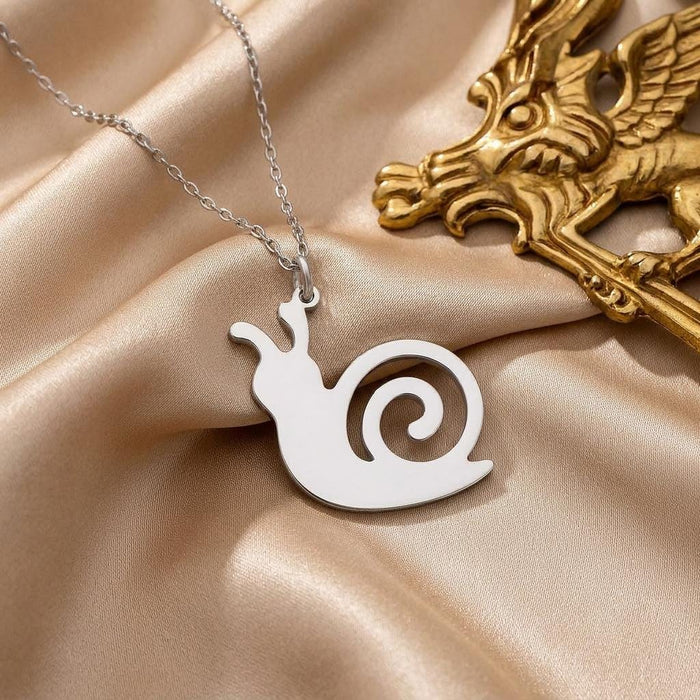 Silver snail pendant with an open spiral-shell cutout on champagne satin beside a gold decorative object