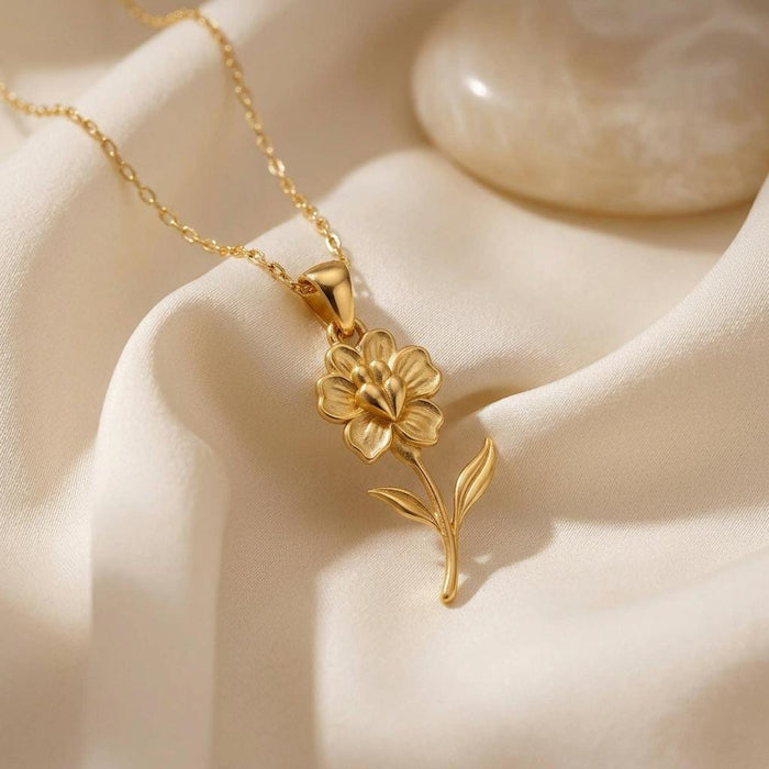 Gold Plated Silver Snapdragon Flower Necklace with a layered bloom and two-leaf curved stem on ivory satin beside a pearl