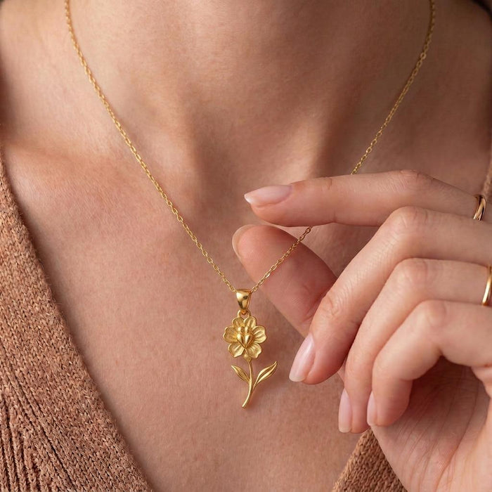 Close view of a Gold Plated Silver flower-and-stem necklace worn at the neckline with a hand beside the pendant