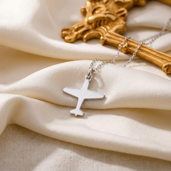 Airplane pendant necklace displayed on cream satin beside a decorative gold frame