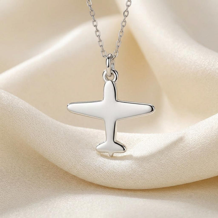 Close-up of the polished airplane pendant and chain on cream satin