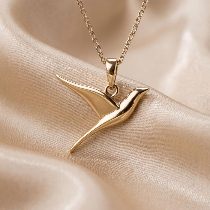 Gold Plated Silver swallow pendant necklace with swept wings and pointed tail on champagne satin
