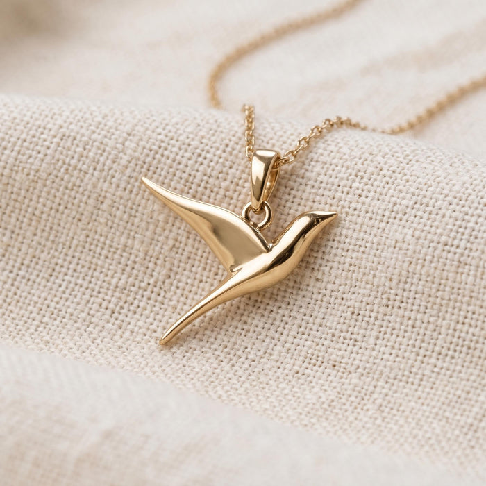 Gold Plated Silver swallow pendant necklace displayed on textured cream fabric