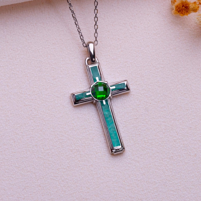 Rectangular aventurine cross necklace with teal inset panels and a round green center stone on pale textured fabric