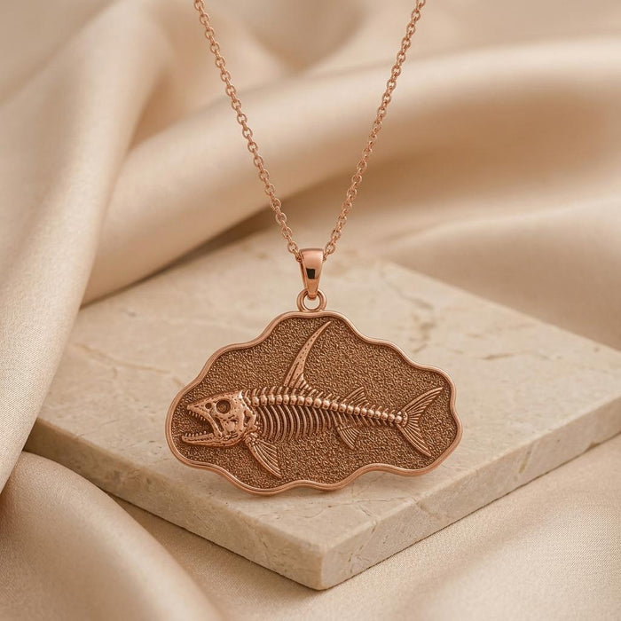 Rose Gold Plated Stethacanthus fossil pendant necklace on a pale stone slab with beige satin