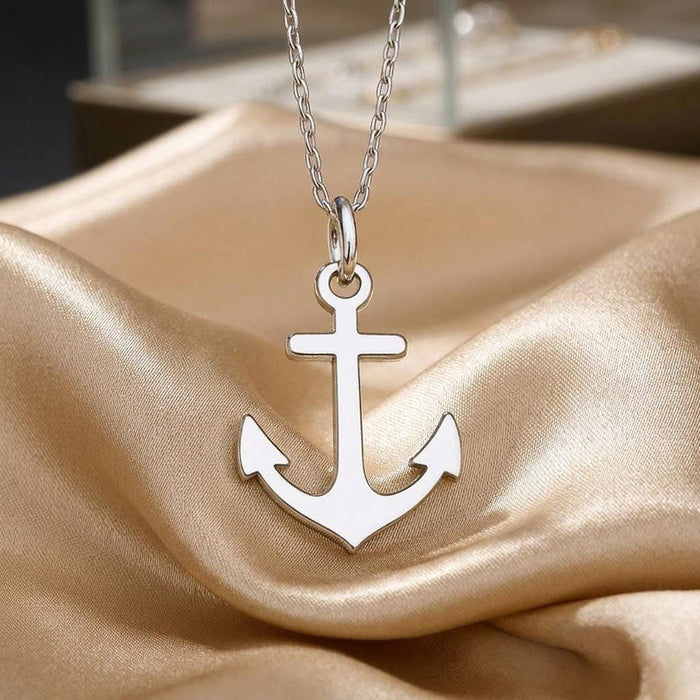 Polished anchor pendant necklace displayed on draped cream fabric