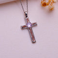 Sunstone Cross Necklace with warm-toned inlay panels and a round center stone on pale pink fabric