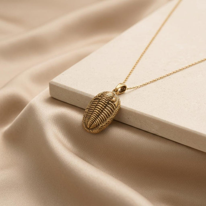 Gold Plated Silver trilobite pendant necklace displayed on a pale stone block and champagne satin