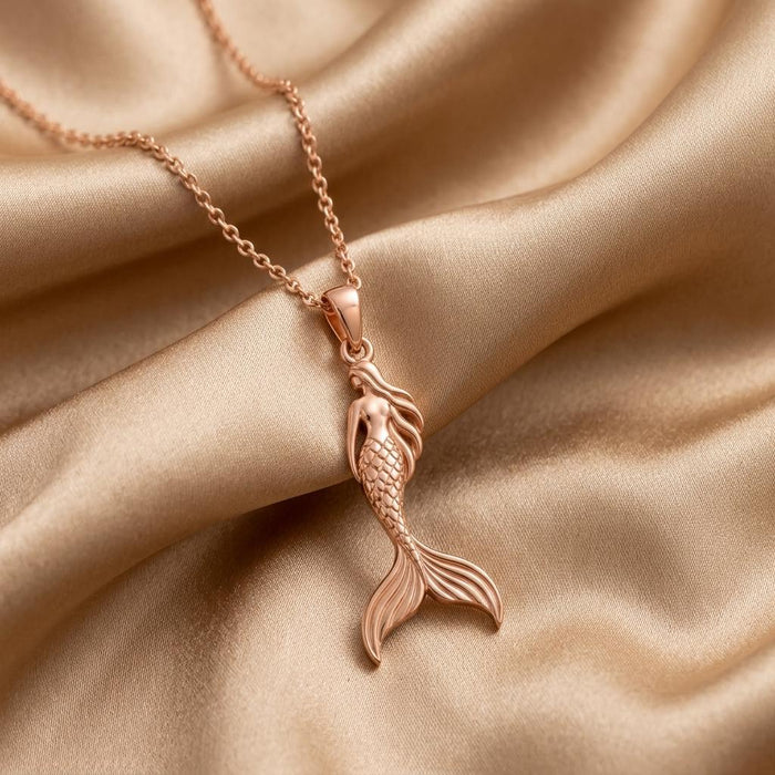 Rose-tone mermaid silhouette pendant necklace arranged on champagne satin